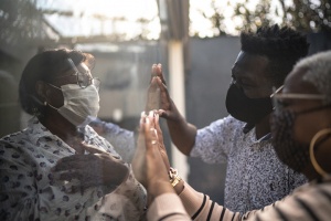 family with face masks touching hands through protective barrier